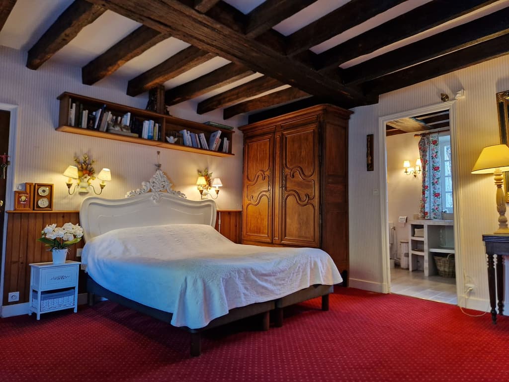 Zimmer mit weißem Bett, altem Eichenschrank, Balken und rotem Teppich