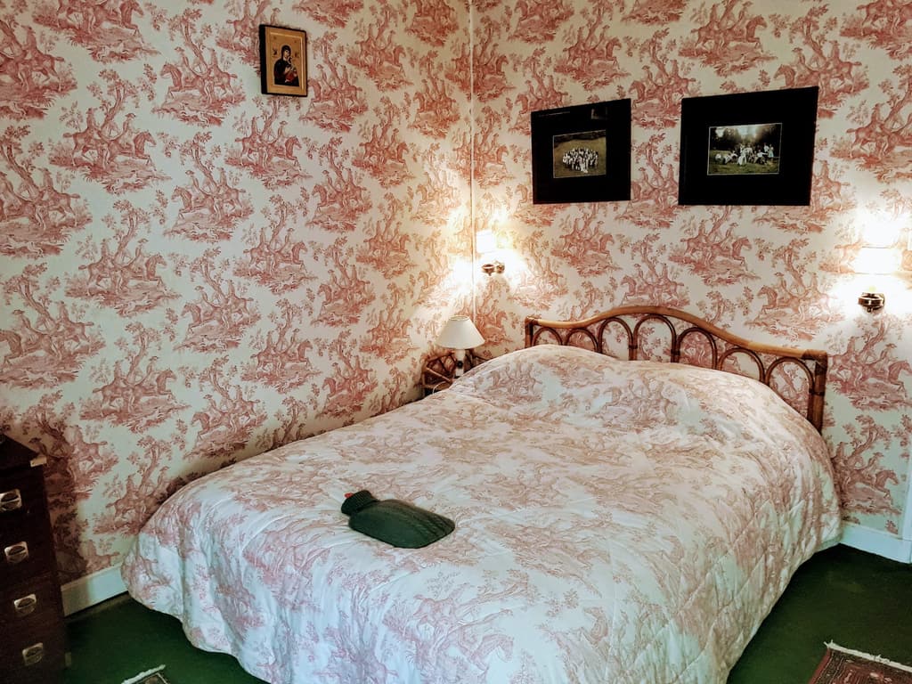 Zimmer mit rosafarbener Toile-de-Jouy-Tapete, schmiedeeisernem Bett und passender Tagesdecke