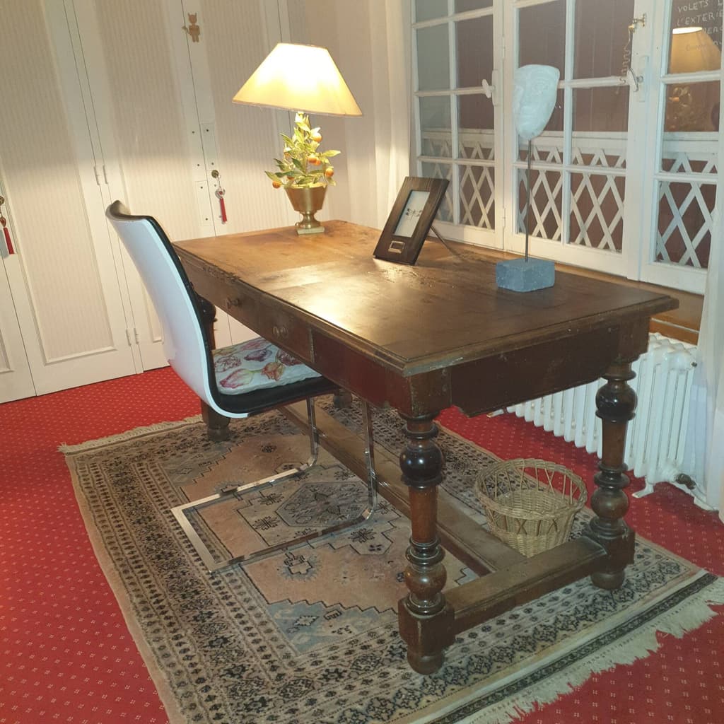 Old wooden desk with a lamp and a chair, in front of glazed doors with glazing bars