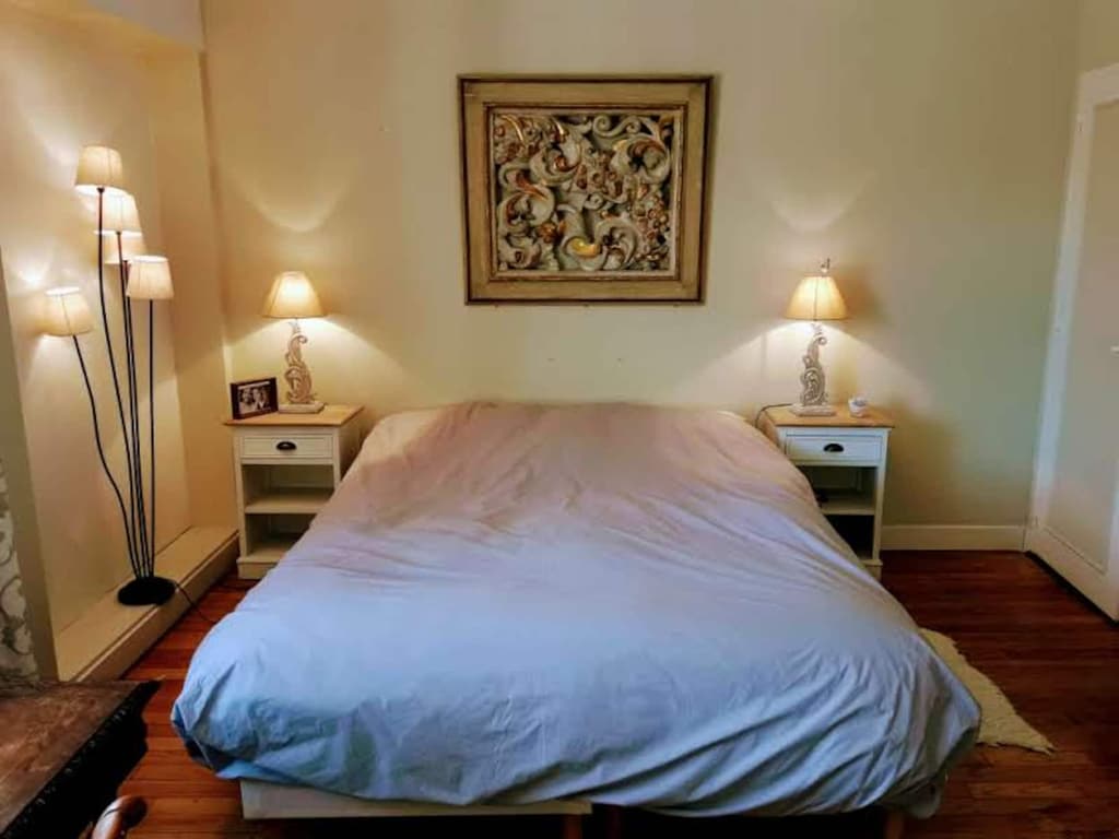 Zimmer mit Doppelbett und blauer Bettdecke, weißen Nachttischen und Stehlampe