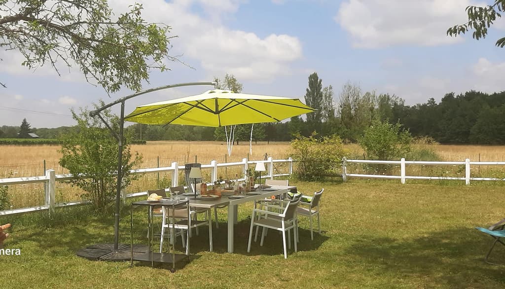 Gedeckter Gartentisch unter einem gelben Sonnenschirm, dahinter die Felder und der weiße Zaun