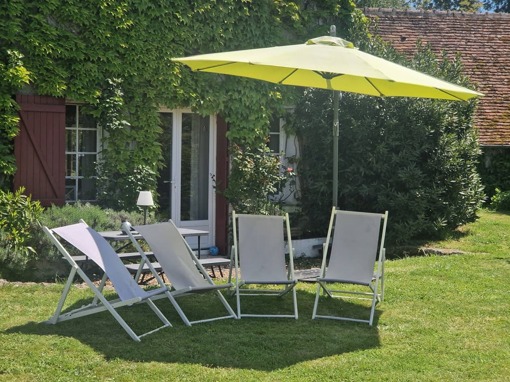 Four sun loungers under a yellow parasol in front of the house