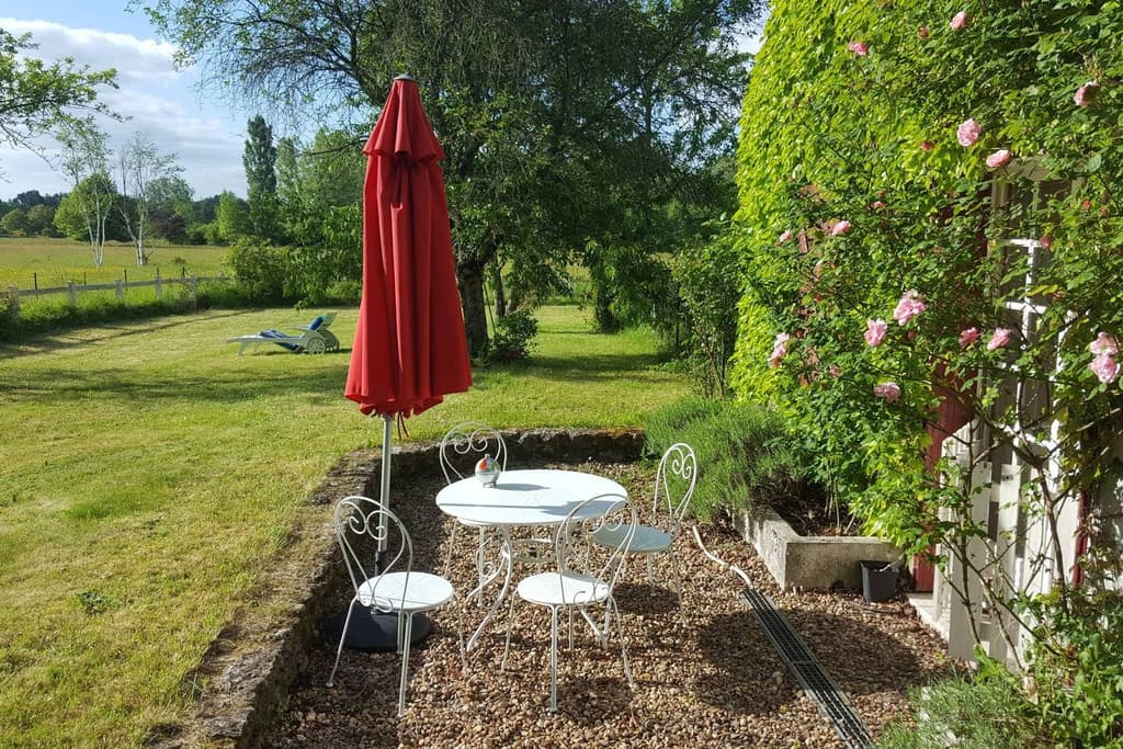 Small white wrought-iron table on the gravel, a closed red parasol and a rose bush