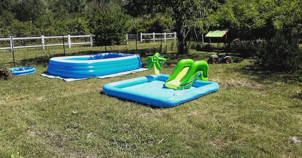 Inflatable paddling pools for children on the lawn, with the white fence behind
