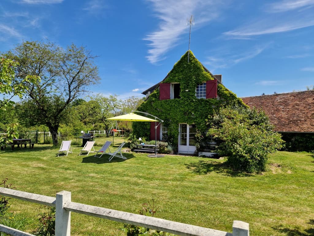 Das efeubewachsene Landhaus mit roten Fensterläden, gelbem Sonnenschirm und Liegestühlen auf dem Rasen