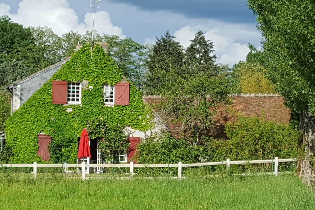 The ivy-covered house behind a white fence, with the meadow in the foreground