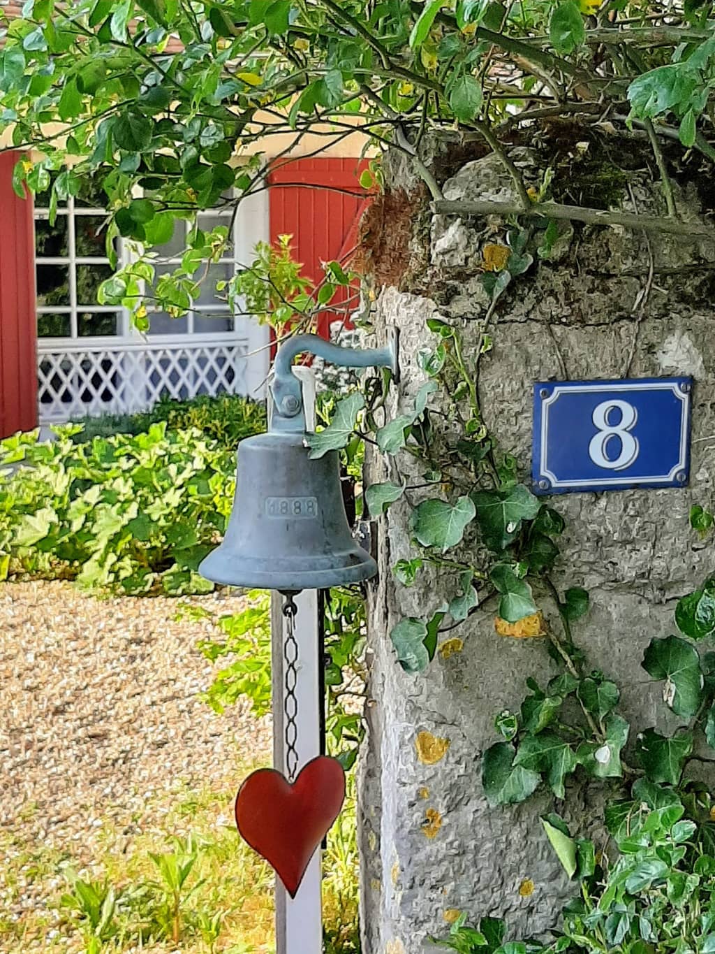 Campanella di bronzo e targa smaltata numero 8 su un pilastro di pietra coperto di edera, cuore rosso