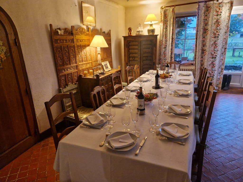 Salle à manger avec longue table dressée, nappe blanche et vaisselier ancien