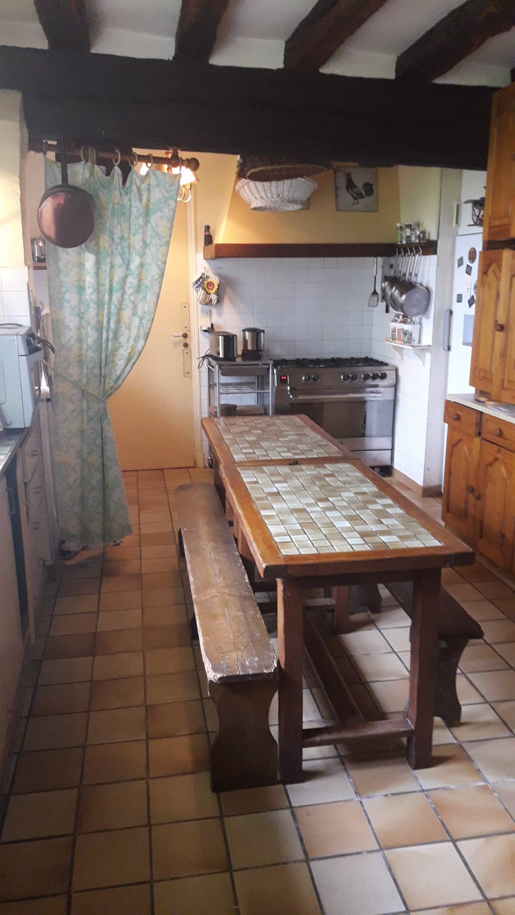 Cucina sotto le travi con grande tavolo piastrellato, panche di legno e cucina a gas
